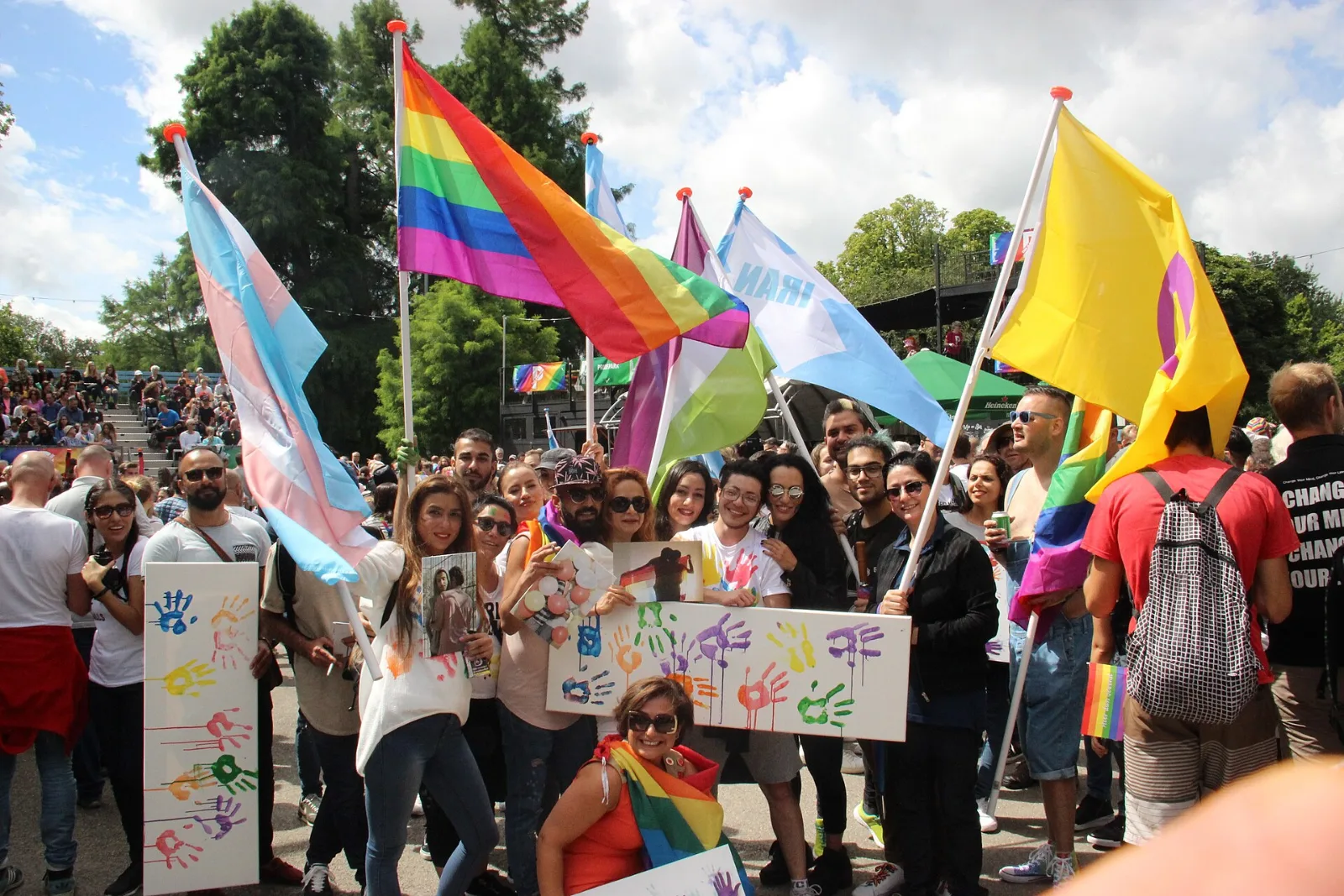 Marchers carrying several Pride flags, among them a lavender, white and green Genderqueer flag.