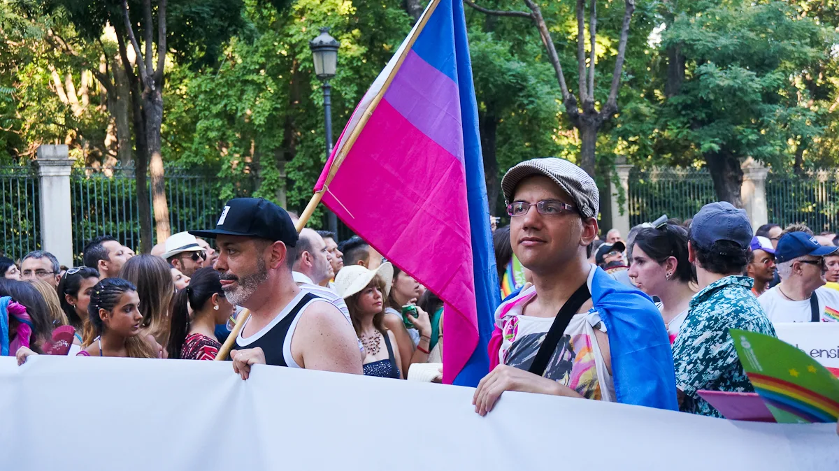 A bisexual flag carried on a pole at a Pride march, hanging with blue at the top, purple in the middle and magenta at the bottom.
