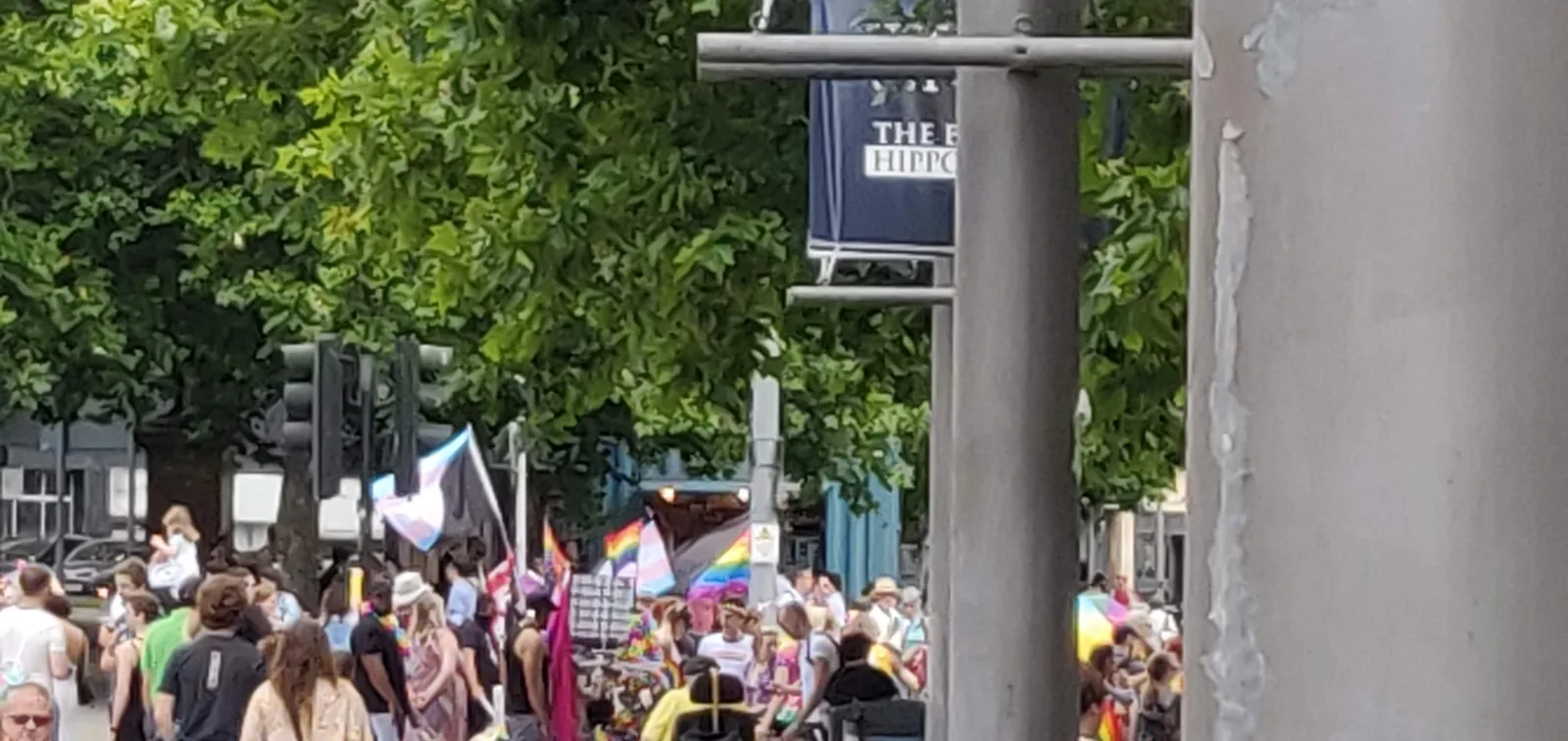 The same Bristol Pride crowd moments later, with the transgender-and-black and rainbow-and-black diagonal flags still visible.