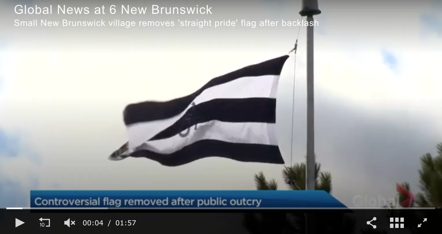 A television news still captioned Global News at 6 New Brunswick, Small New Brunswick village removes 'straight pride' flag after backlash. A flag of black and white horizontal stripes flies from a metal pole against a pale sky, twisted by the wind, with a dark device visible near its centre. A lower-third banner reads Controversial flag removed after public outcry.