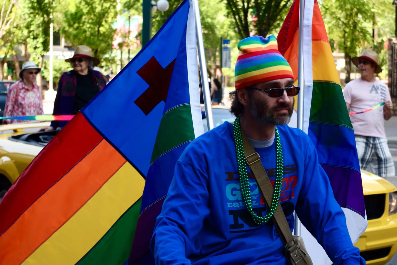 A man riding in the Edmonton Pride Parade carrying the Christian rainbow flag and a plain rainbow flag, one on each side.