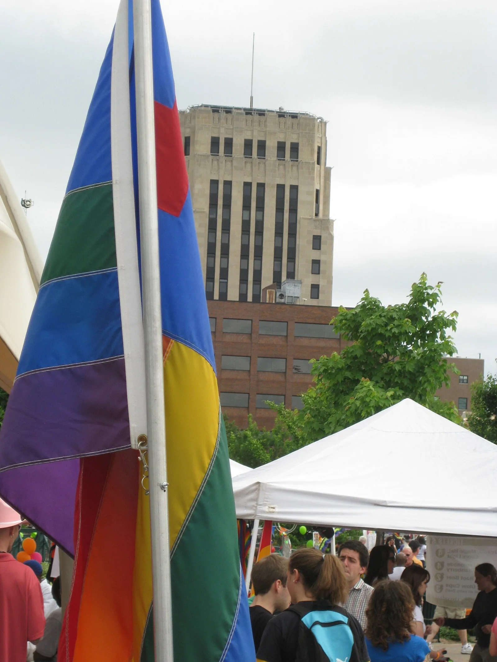 The Christian rainbow flag flying beside a plain six-stripe rainbow flag at Kalamazoo Pride 2011, with a downtown office building behind.