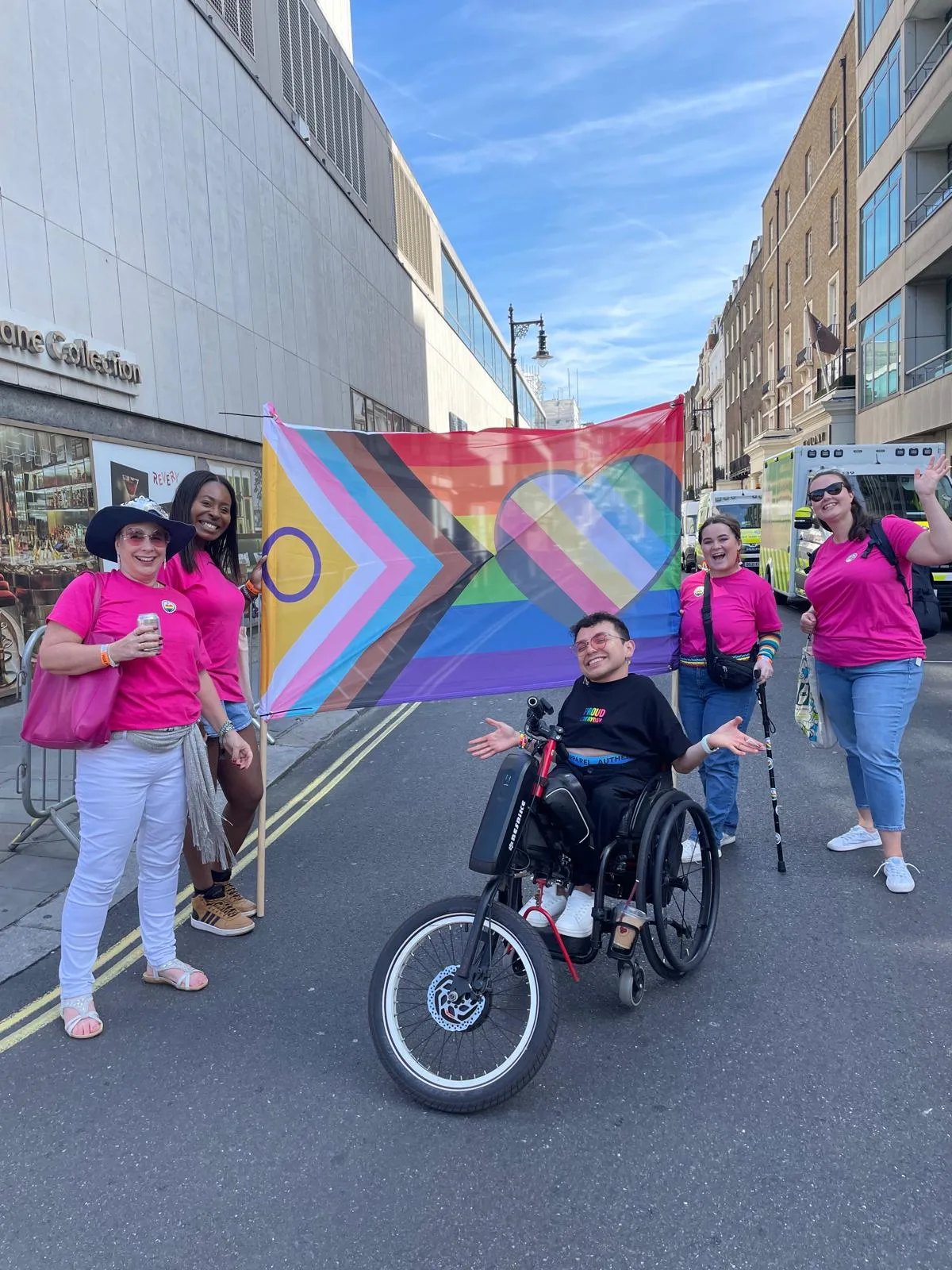 Evenbreak team members in pink t-shirts carrying the Disability-Inclusive Pride Flag in the Pride in London parade on 29 June 2024, walking alongside Valentino Vecchietti, dressed in white