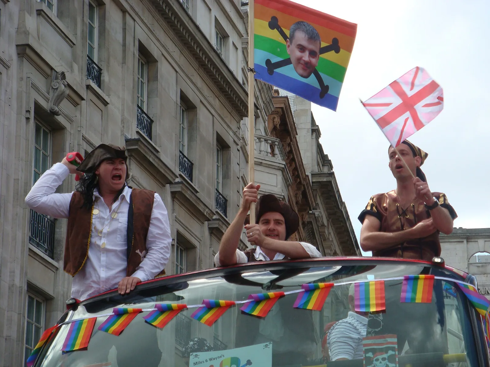 A small Pink Jack hand flag waved from a parade vehicle dressed with rainbow bunting at Pride London.