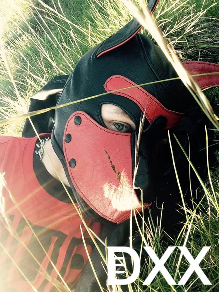 A human pup in a black hood photographed outdoors.