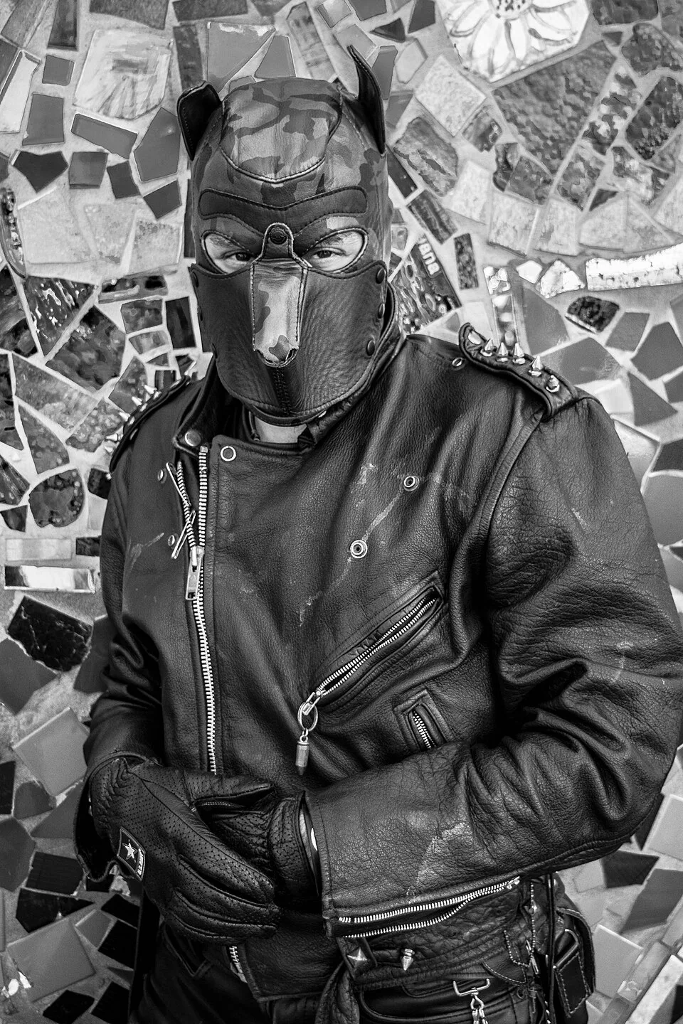 A black and white portrait of a man in a leather puppy mask and motorcycle jacket.