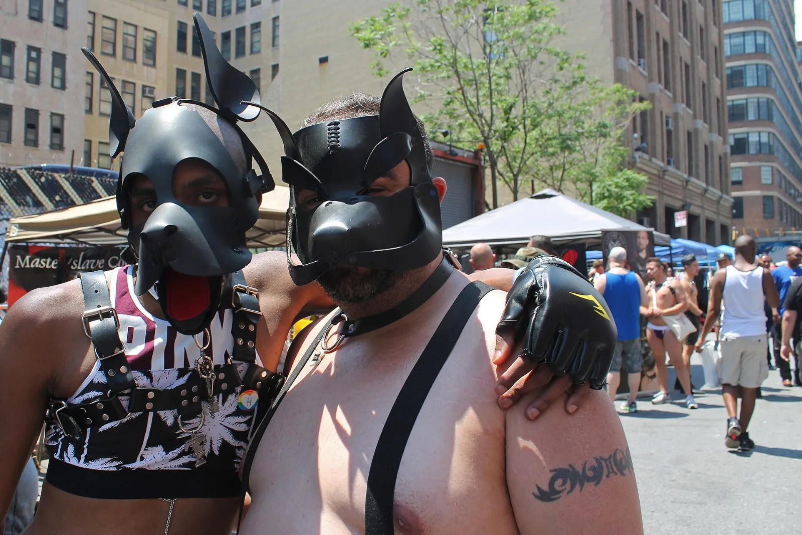 Two people in black pup hoods standing together at an outdoor street festival.