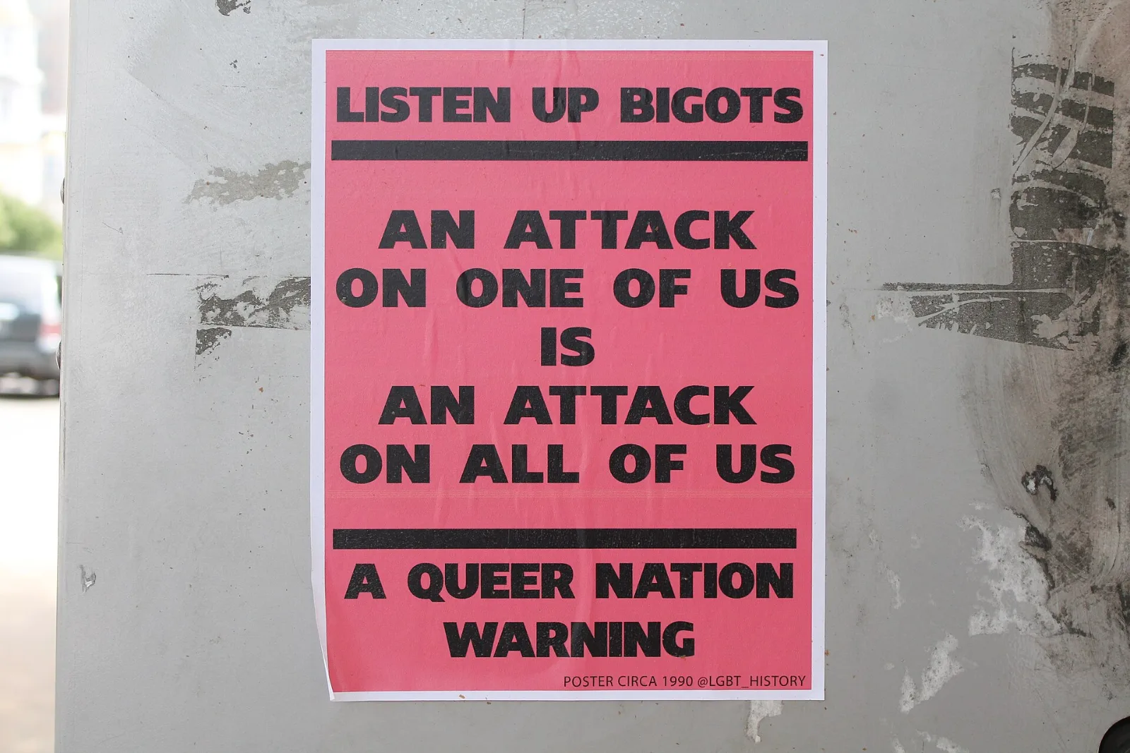 A pasted street poster on a wall reading LISTEN UP BIGOTS, AN ATTACK ON ONE OF US IS AN ATTACK ON ALL OF US, A QUEER NATION WARNING, photographed at Lafayette Park in Washington DC.