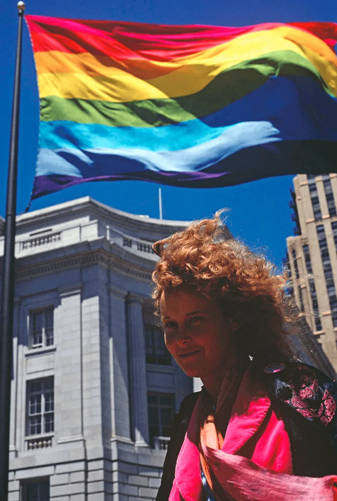 Lynn Segerblom, known as Faerie Argyle Rainbow, standing in front of one of the original eight-color rainbow flags at United Nations Plaza in 1978.