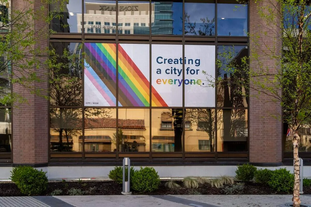 A large white sign in a Boise City Hall window showing diagonal Progress Pride stripes beside the words 'Creating a city for everyone', the last word lettered in rainbow colors.