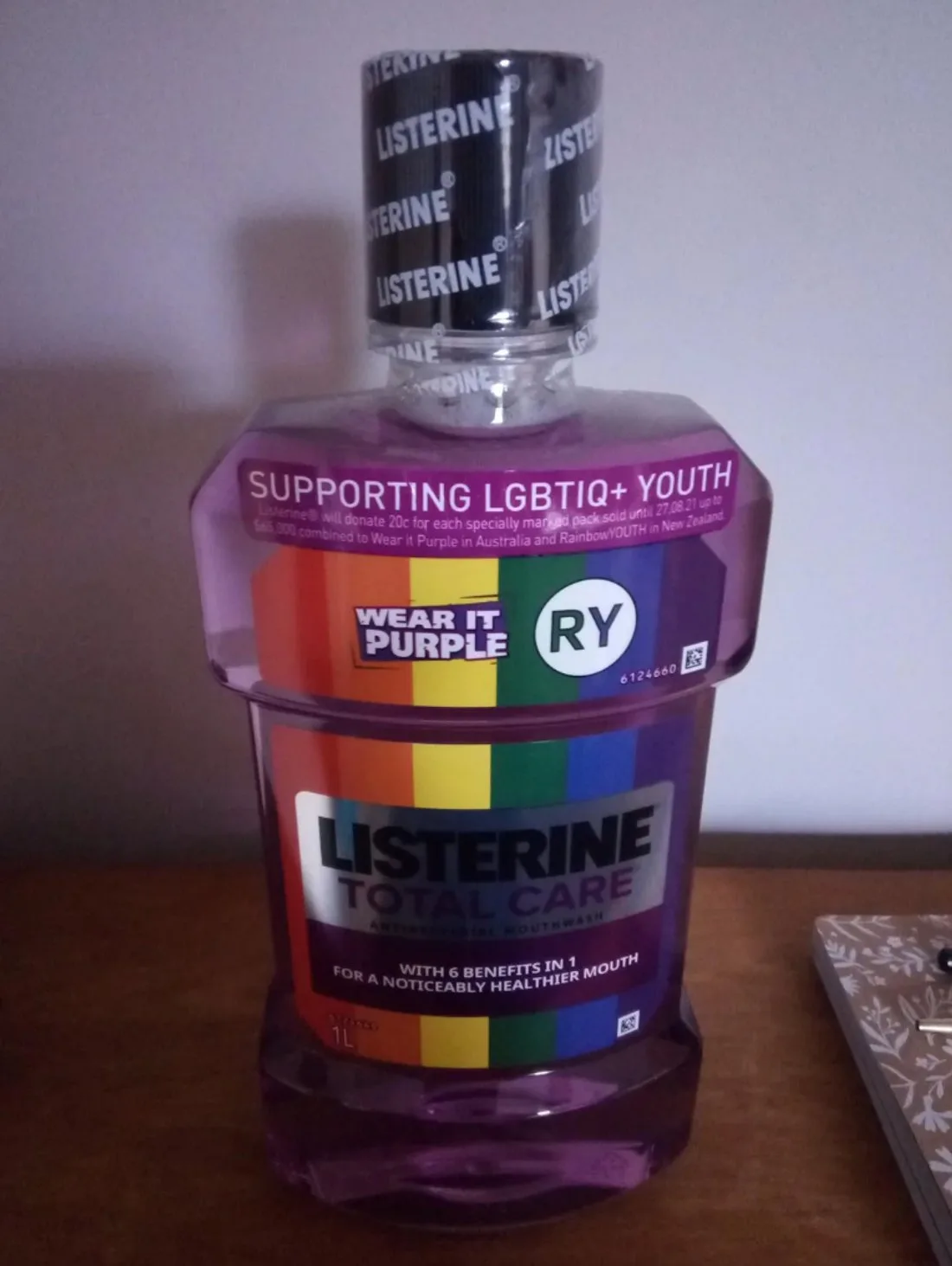 A one-liter Listerine mouthwash bottle with a vertical rainbow-striped label reading 'Supporting LGBTIQ+ Youth,' with Wear It Purple and RainbowYOUTH logos, photographed on a wooden table.