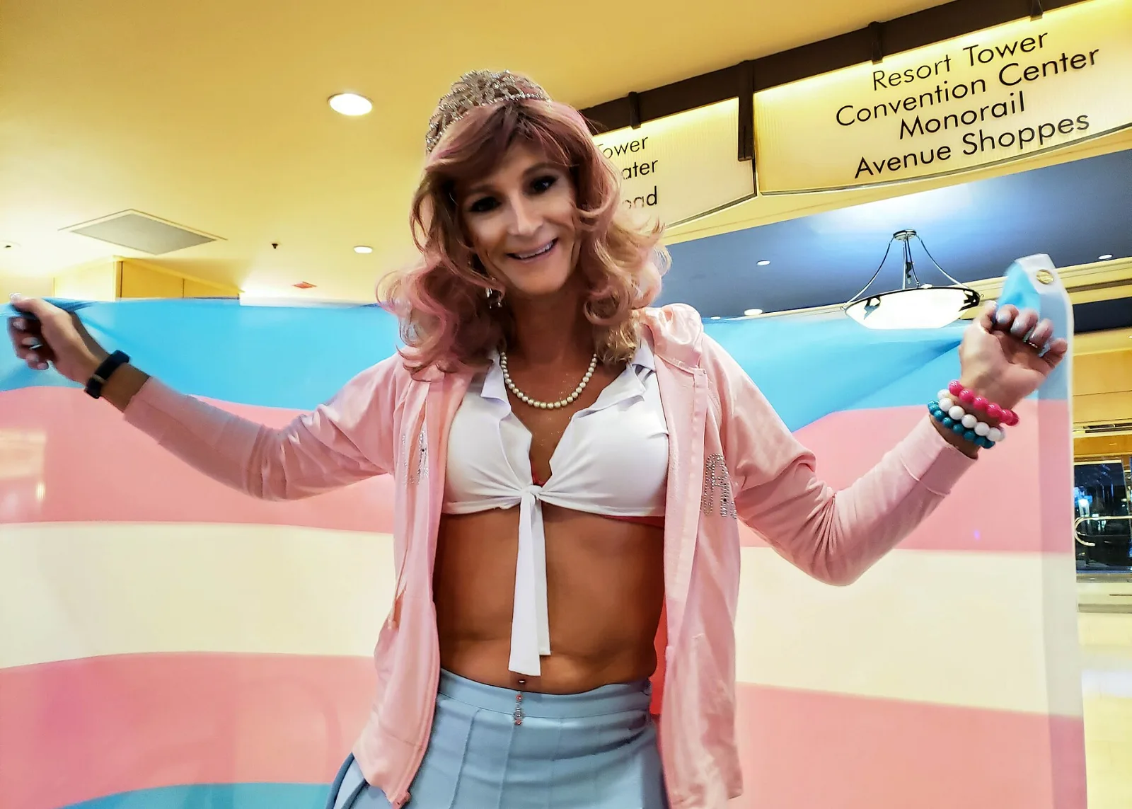 A person holding an open transgender pride flag indoors at a hotel.