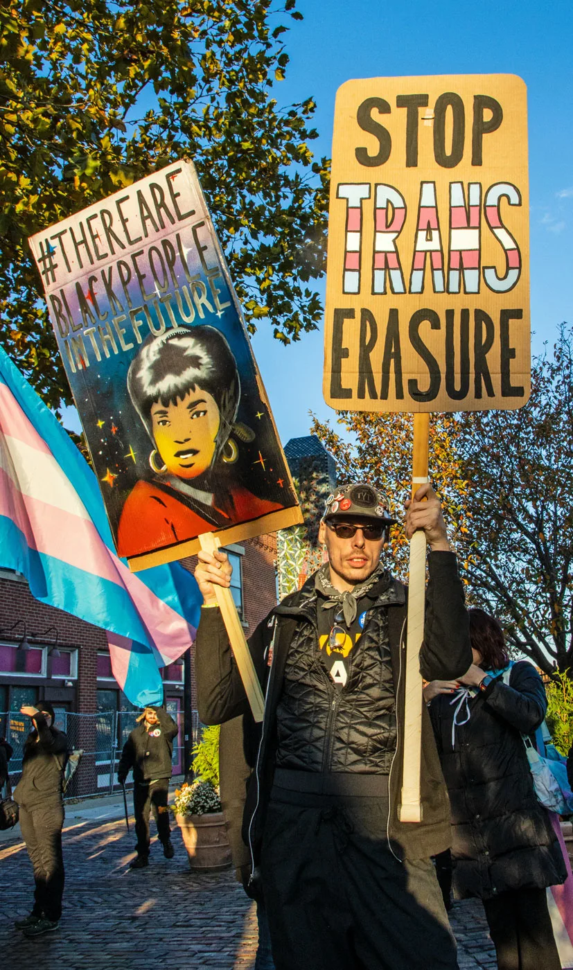 A marcher holding a transgender pride flag above their head in a street demonstration.