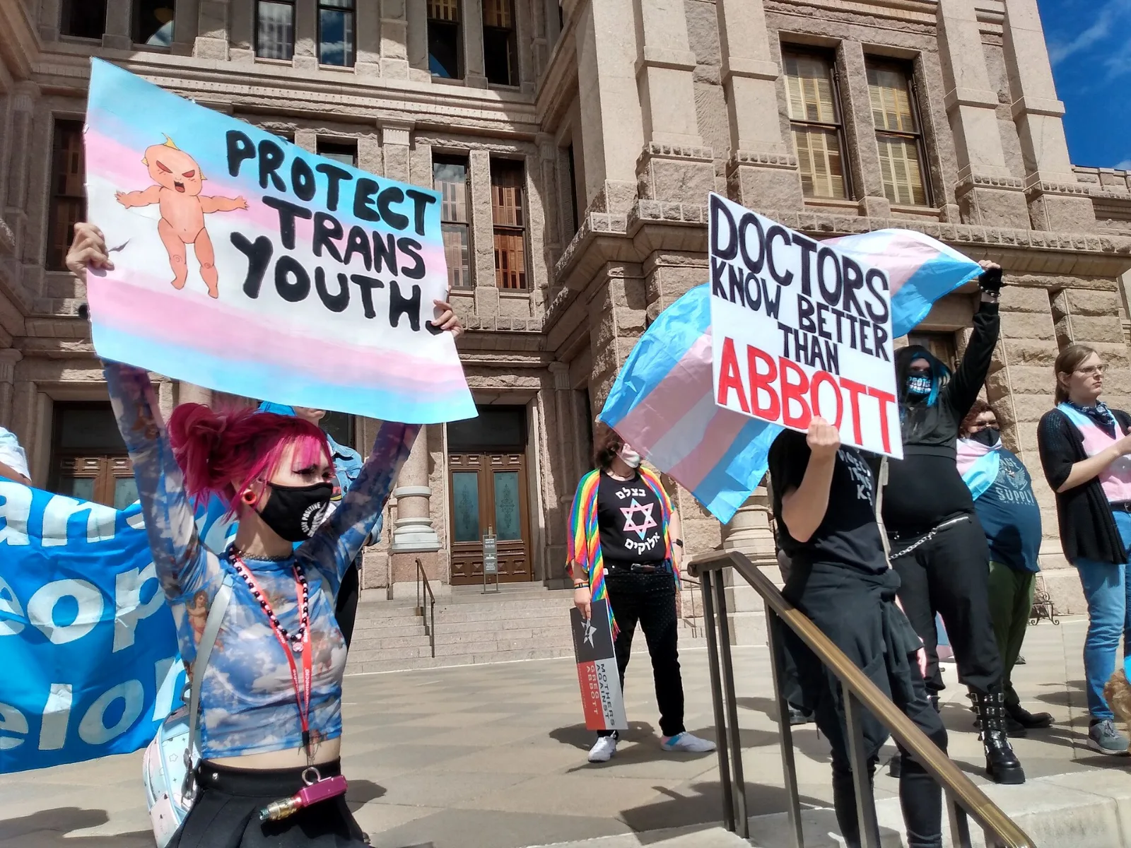 Demonstrators with transgender pride flags and placards, one bearing a Star of David.