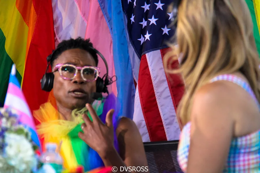 A parade float or open vehicle with participants and flags, including a transgender pride flag and the flag of the United States.