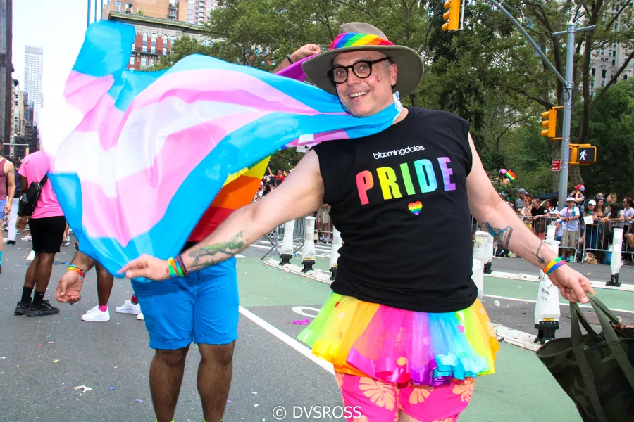 Parade marchers in rainbow clothing, a transgender pride flag among the banners.