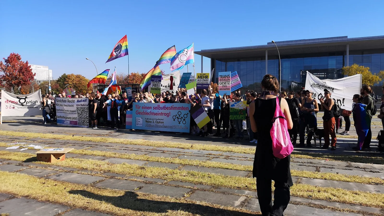 A rally in front of the German Chancellery with pride flags raised, one charged with the transgender symbol.