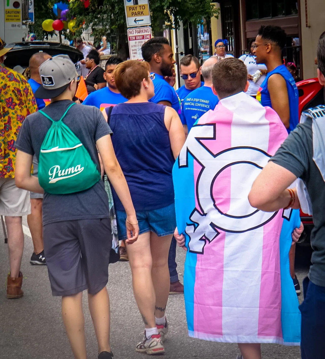 A transgender pride flag carried in a parade with a large transgender symbol, white outlined in black, across its center.