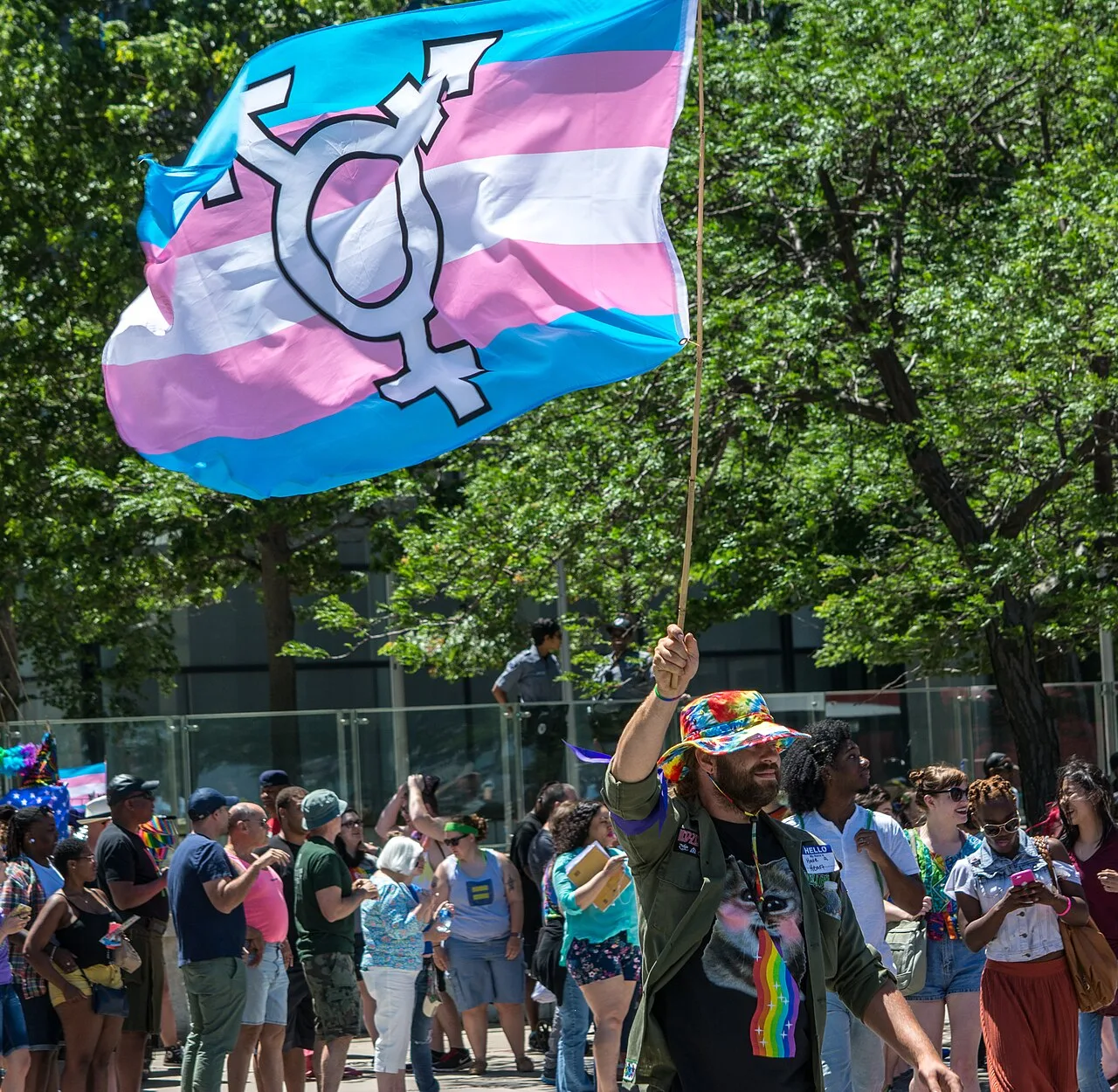 A transgender pride flag with the transgender symbol on it, held up at the end of a parade.