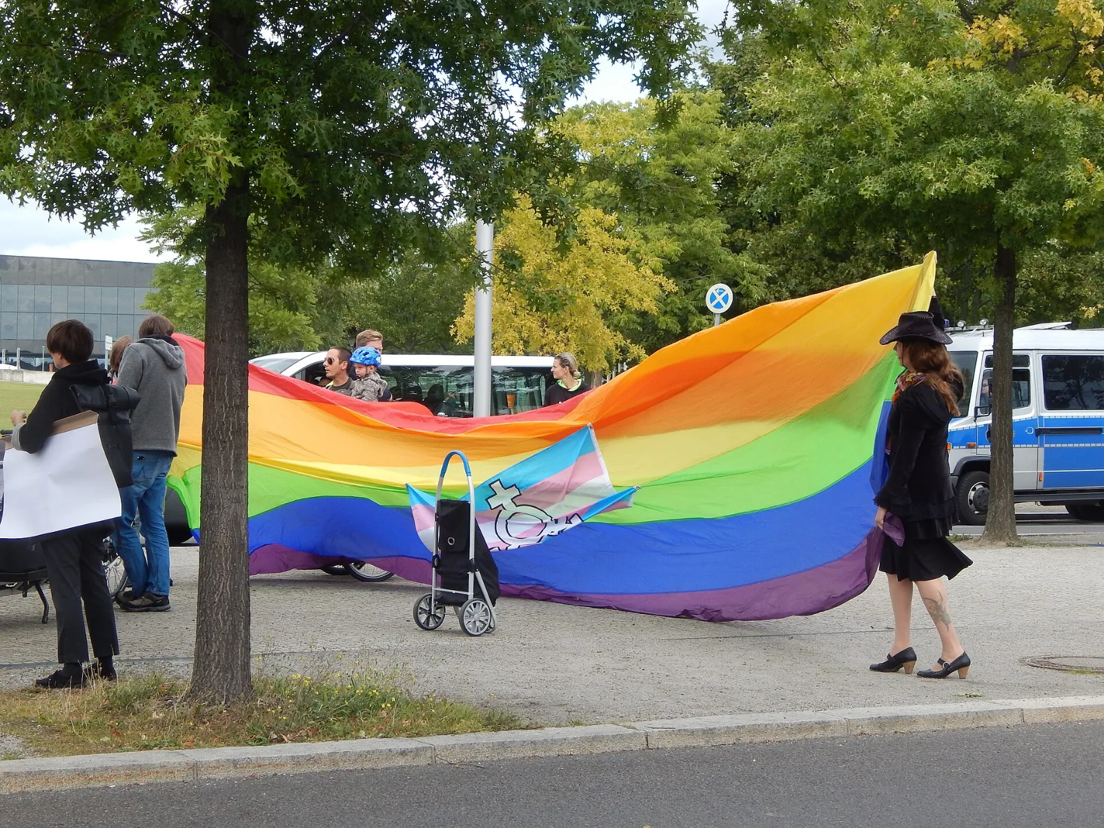 A protest crowd in front of the German Chancellery, a transgender flag bearing the transgender symbol among the banners.