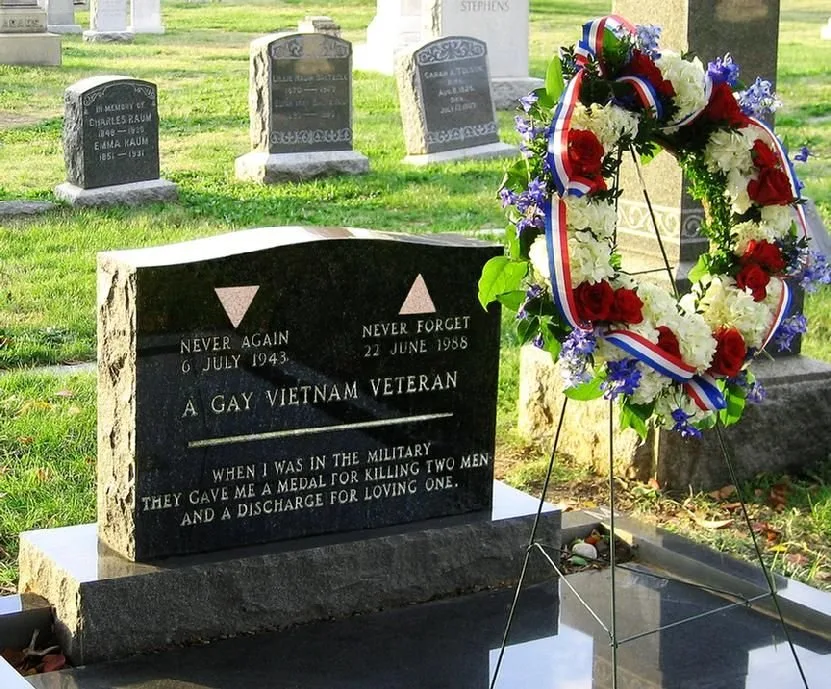 Matlovich's black granite headstone at Congressional Cemetery with a red, white and blue wreath on a stand beside it: two pink triangles, 'Never Again — Never Forget,' 'A Gay Vietnam Veteran,' and the epitaph.