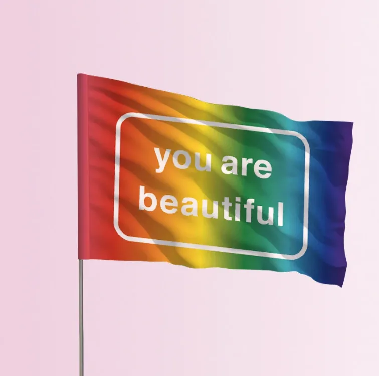 The You Are Beautiful Pride flag on a flagpole: a rainbow gradient with "you are beautiful" in a white rounded frame.