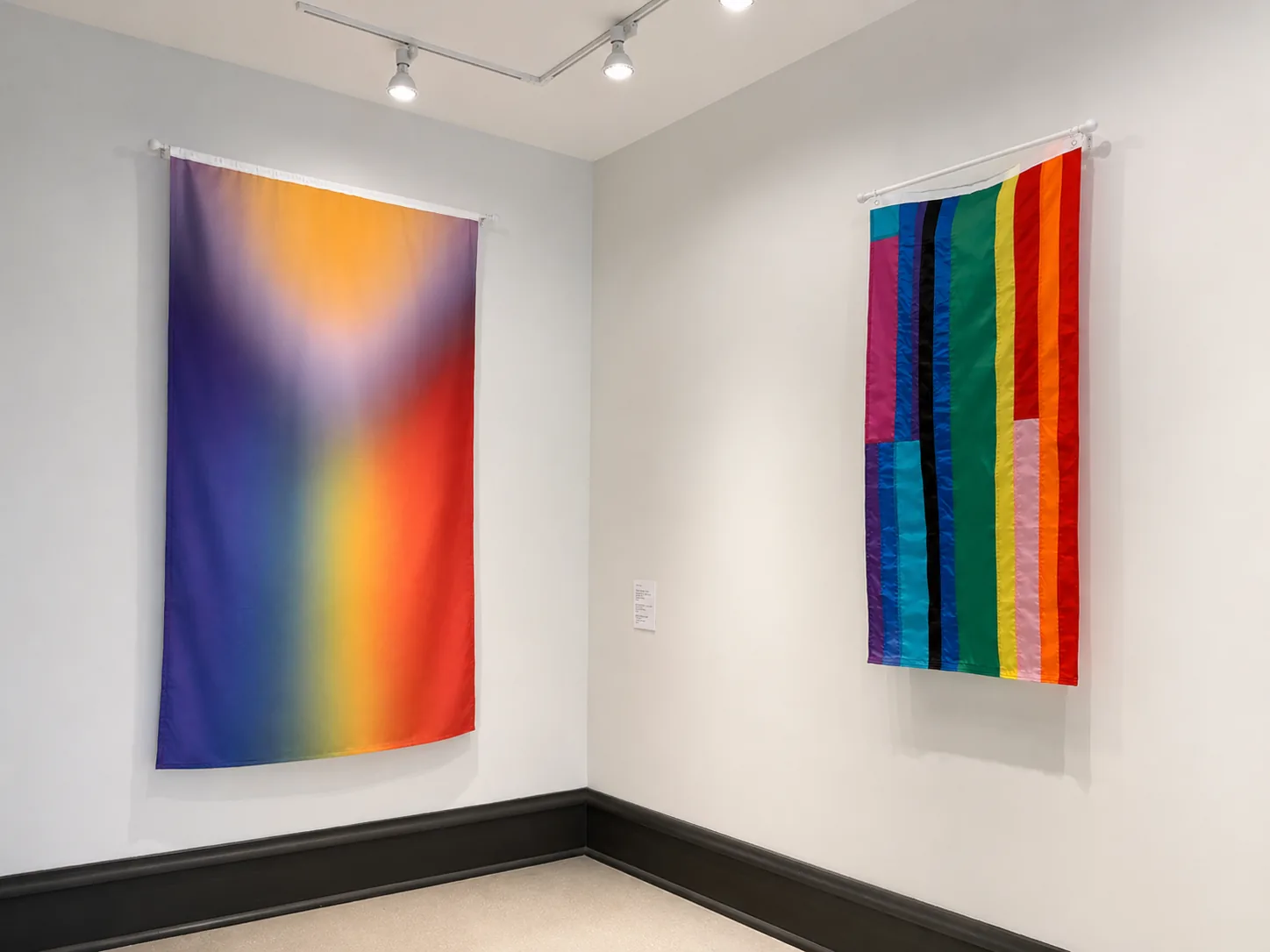 Right to Assemble installation view: the 5790/2029 Pride Flag hung as a tall gradient banner, meeting Utopian Pride Flag #25, a flag sewn from recycled pride flags, in the gallery corner.