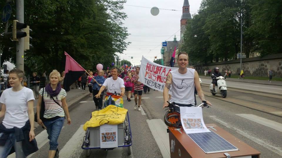 Marchers on Mannerheimintie at Helsinki Pride, a pink and black diagonal flag among them.