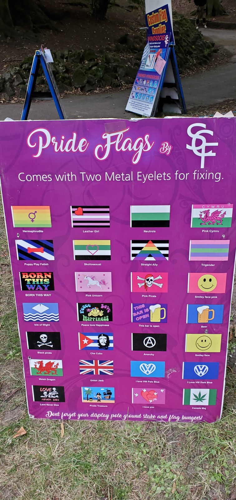 A vendor's sample board of small pride flags, one labelled Skoliosexual with a pink heart outline on yellow, green, white and black stripes.