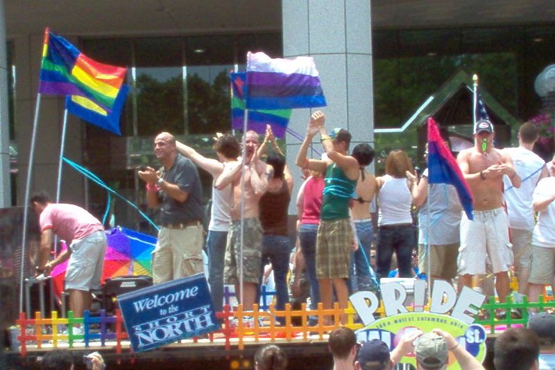A parade float with a five-stripe flag showing white, purple, black and blue below a furled top stripe.