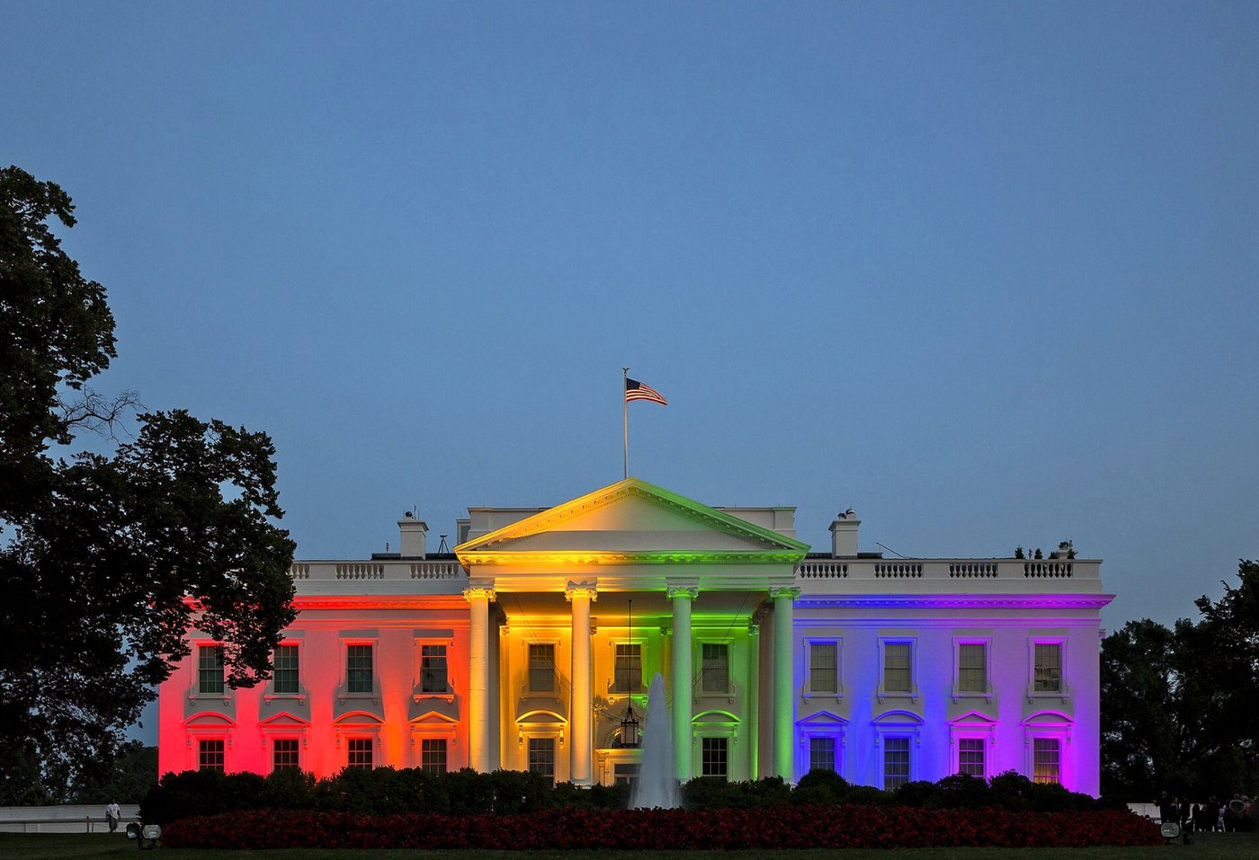 The White House illuminated in the six rainbow flag colors at dusk on June 26, 2015, with the American flag flying above the portico.