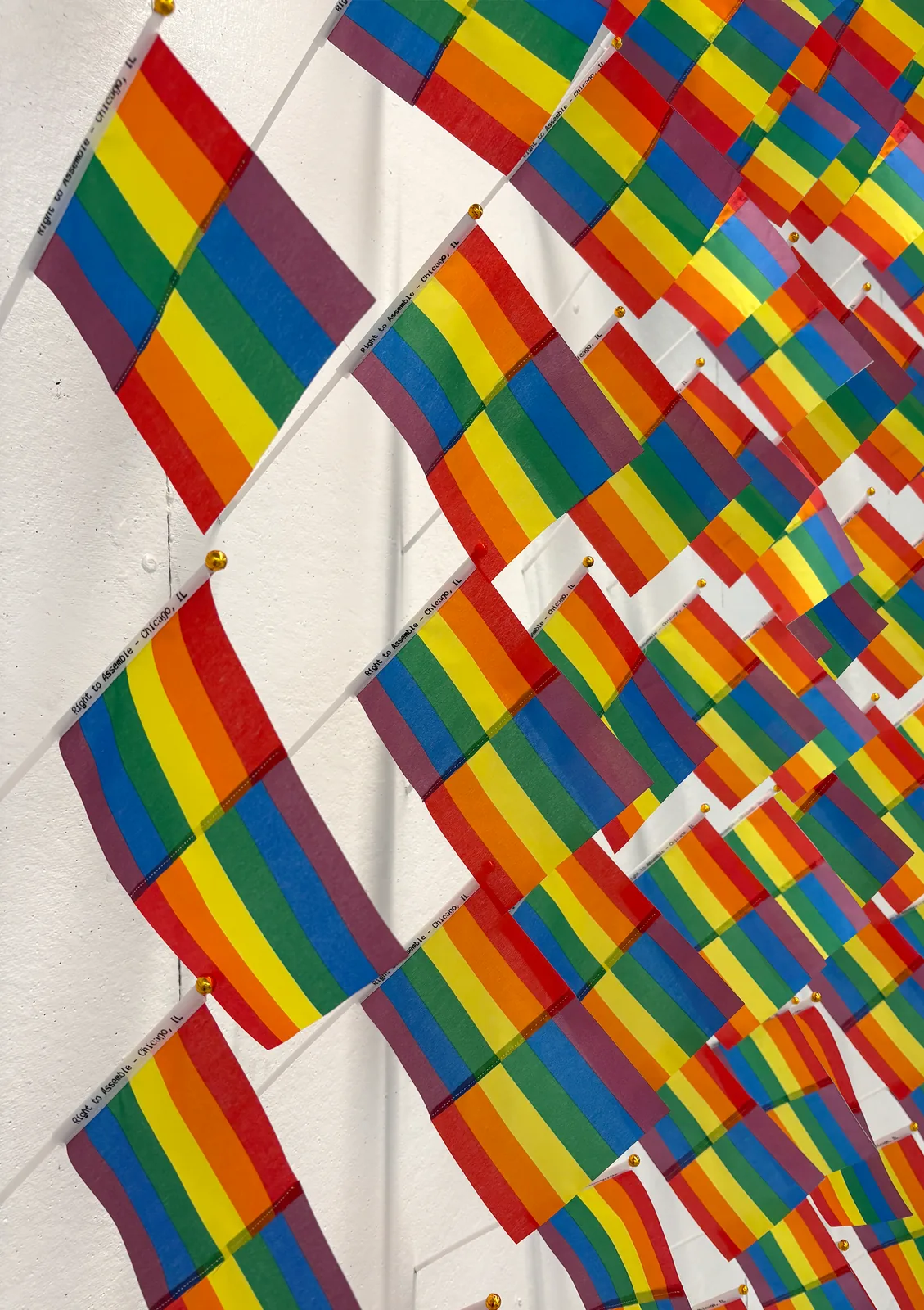 Close-up of the Hand-held Pride Heraldry Flags installation: rows of small inverted, silkscreened nylon pride flags along a gallery wall.