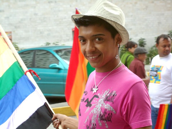 A marcher at Guatemala Pride 2010 carrying a rainbow flag whose lowest stripe is black and whose violet stripe has faded to near-white.